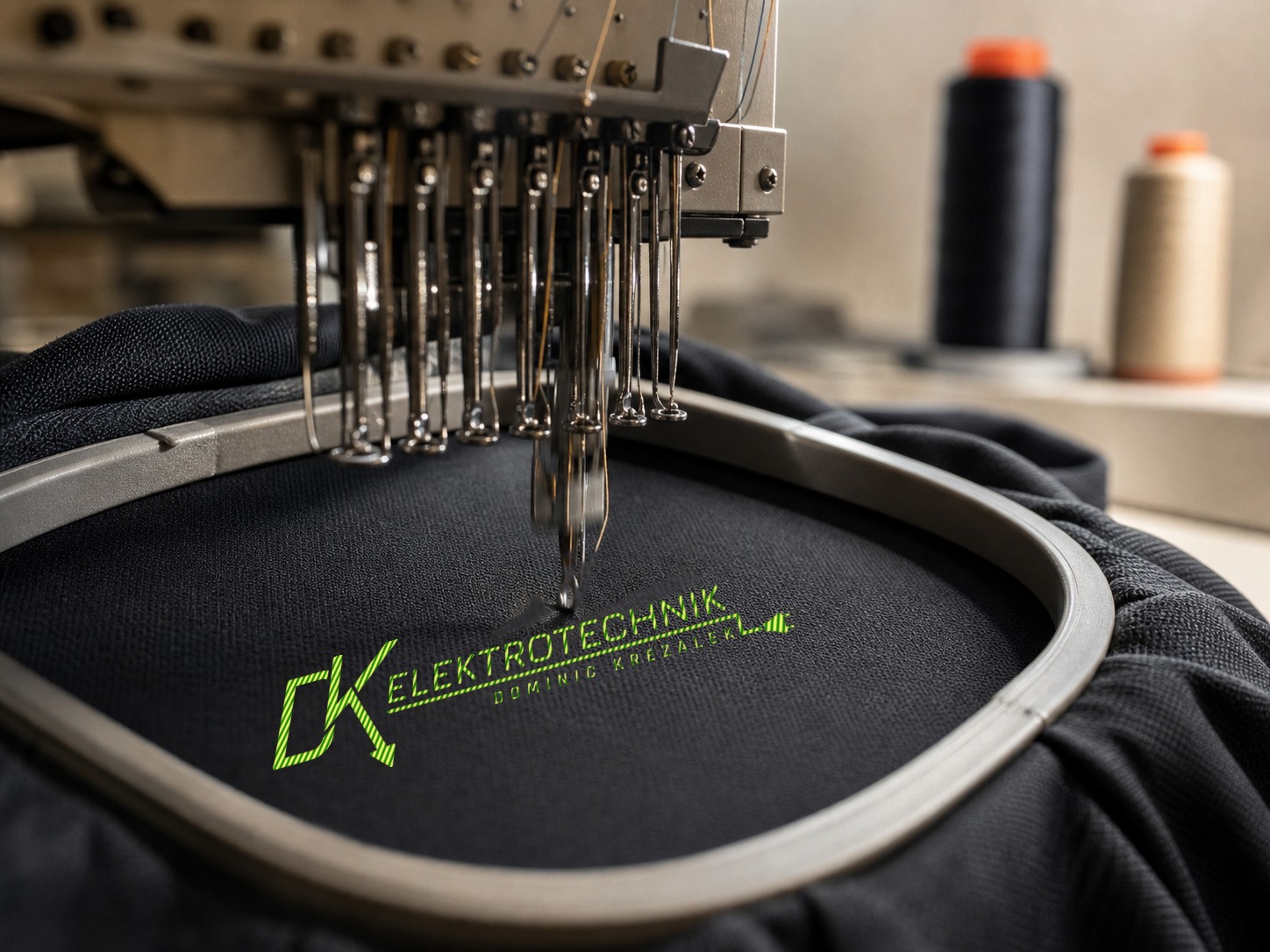 Stickmaschine stickt das Logo von DK Elektrotechnik auf ein schwarzes Arbeitsshirt